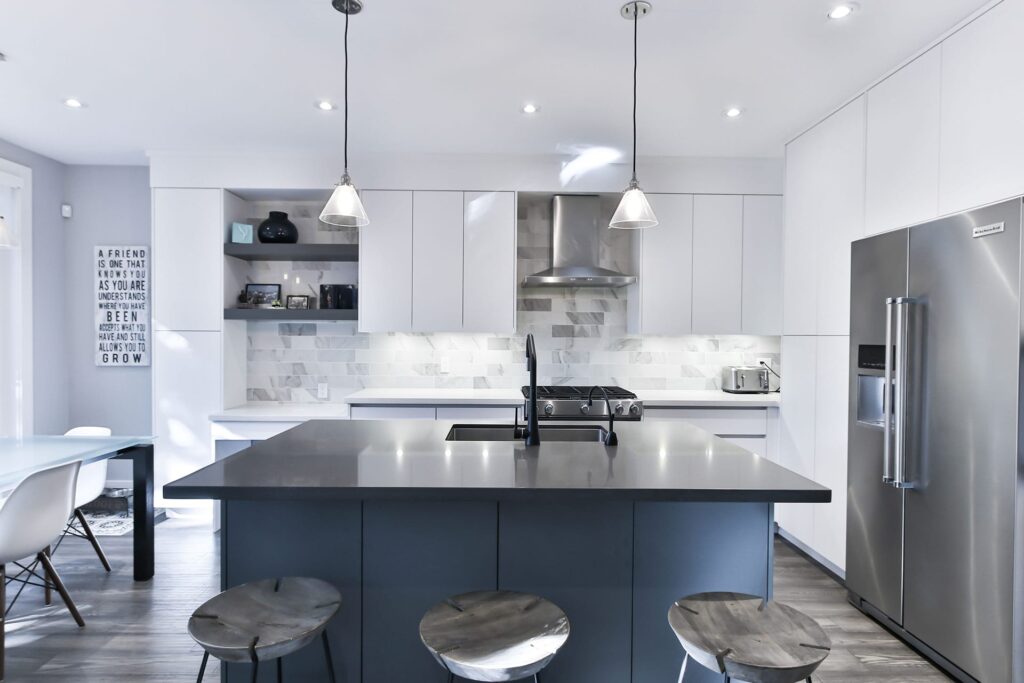 Modern kitchen with a dark gray island, white cabinets, and stainless steel appliances including a large fridge and range hood.