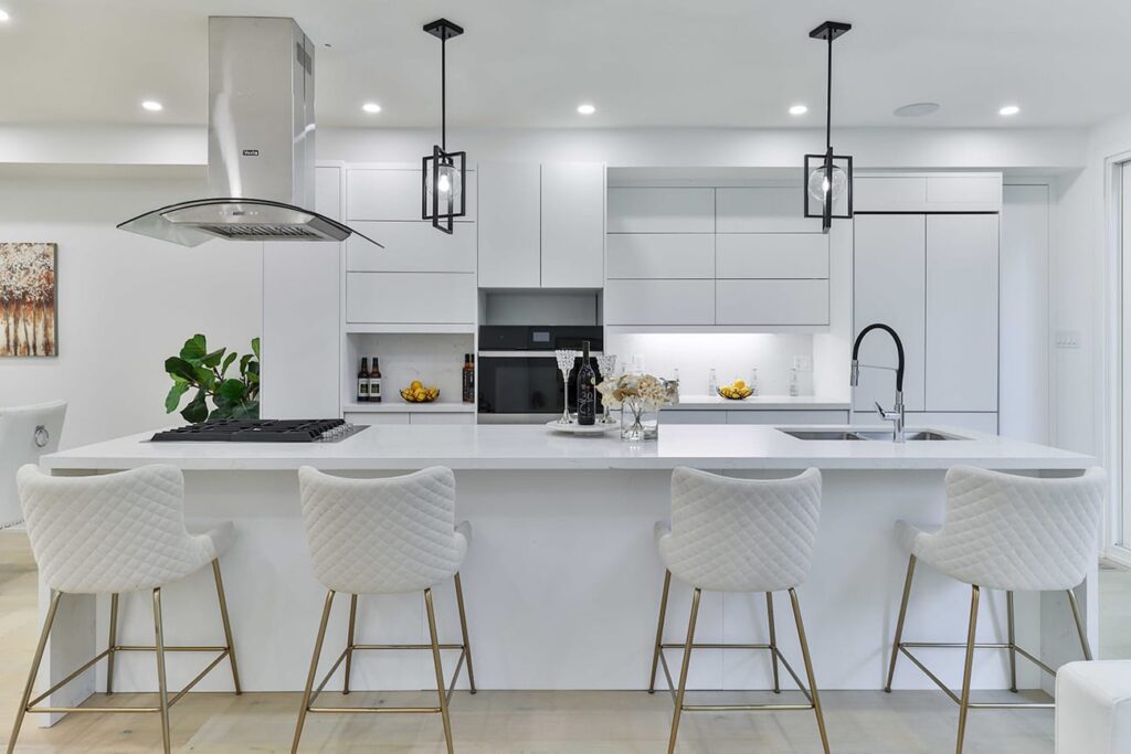 Modern white kitchen with a large island, four quilted bar stools, and a stainless range hood above the stove.